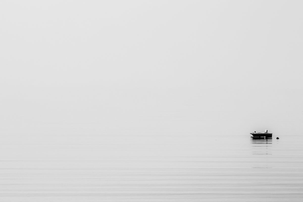 Minimalist monochrome photograph of a boat in the water with fog all around