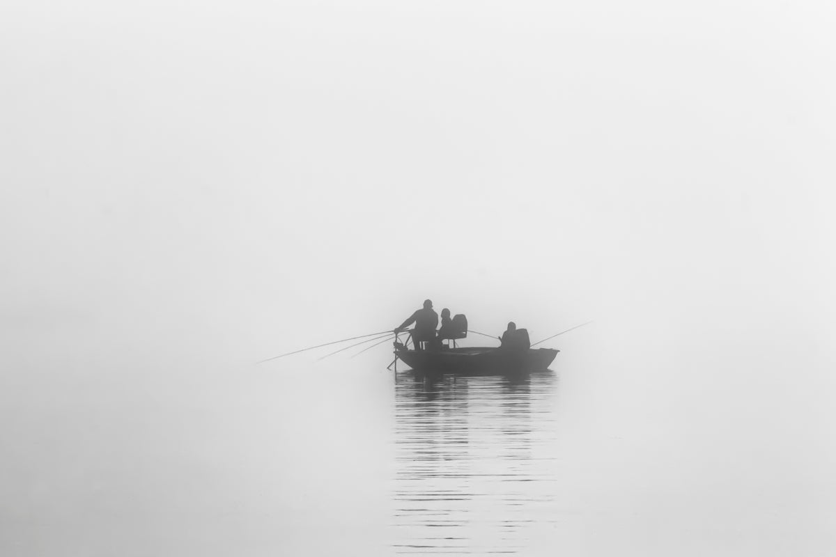Two kids fishing with their father on a cold winter morning in dense fog